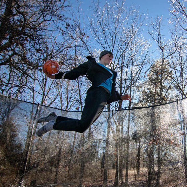 Garçon sautant sur un trampoline ACON avec un ballon de basket à la main