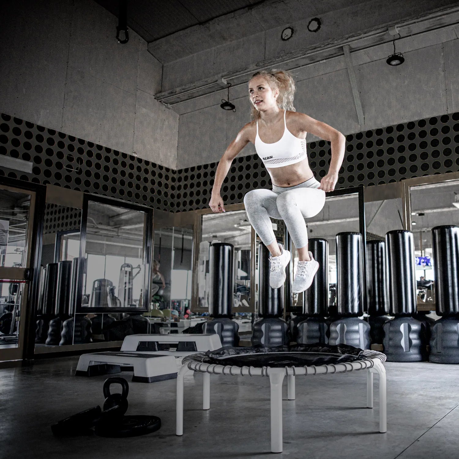 Athlète sautant sur le trampoline de fitness rond ACON Fit 1,12 m avec poignée Active dans une salle de sport.