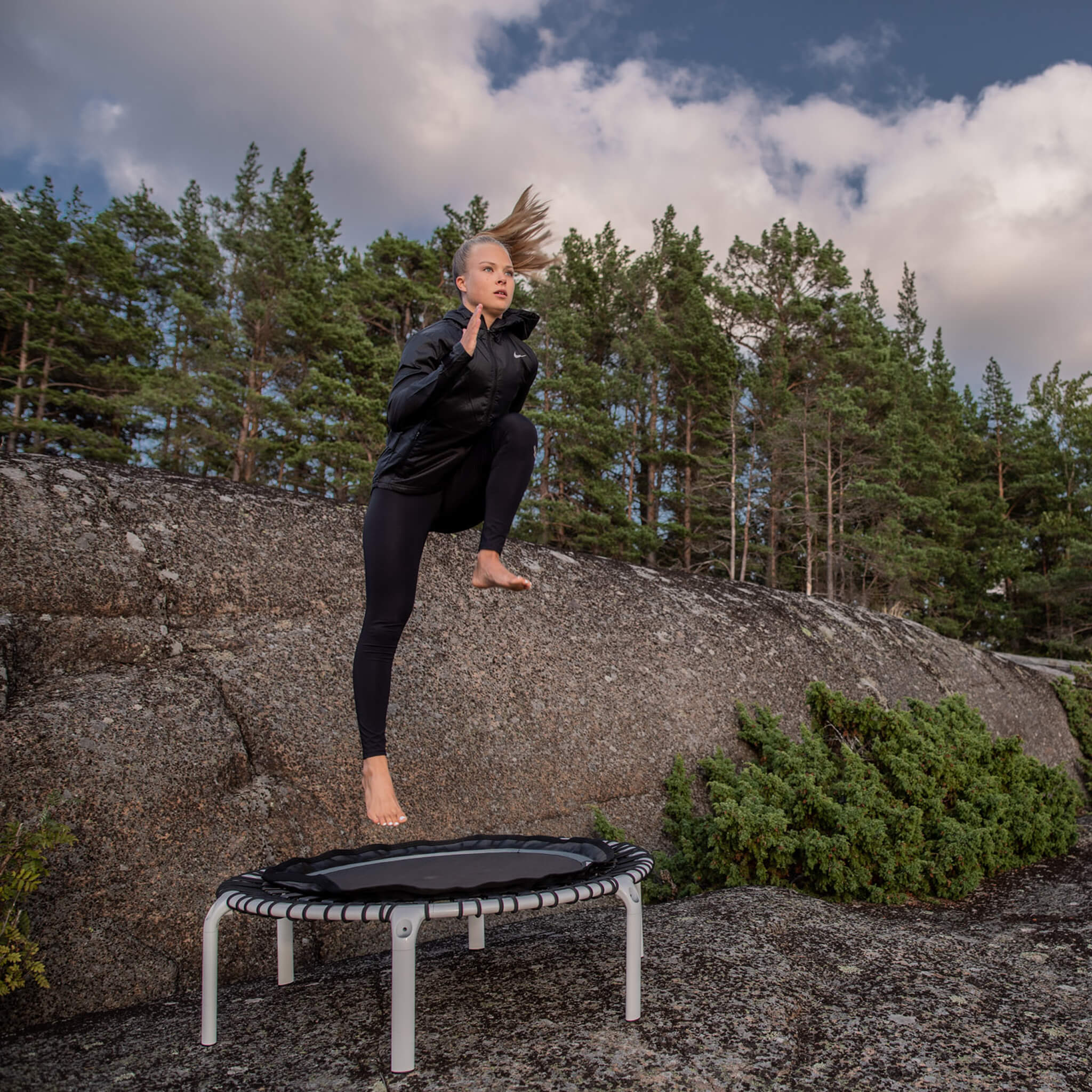 Une femme saute sur un trampoline Acon FIT blanc dans un paysage forestier nordique.
