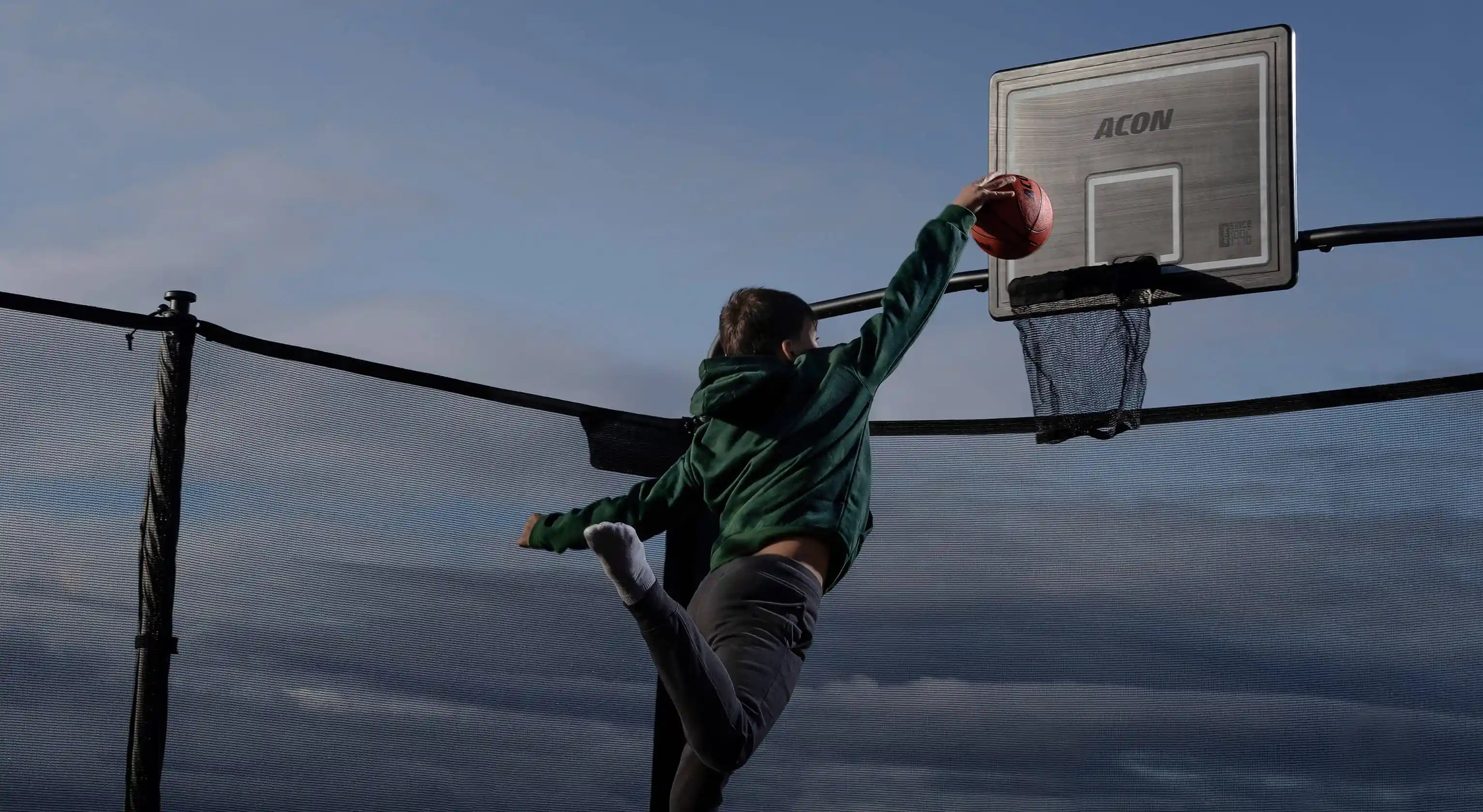 Un garçon lance un ballon de basket dans le panier du trampoline.