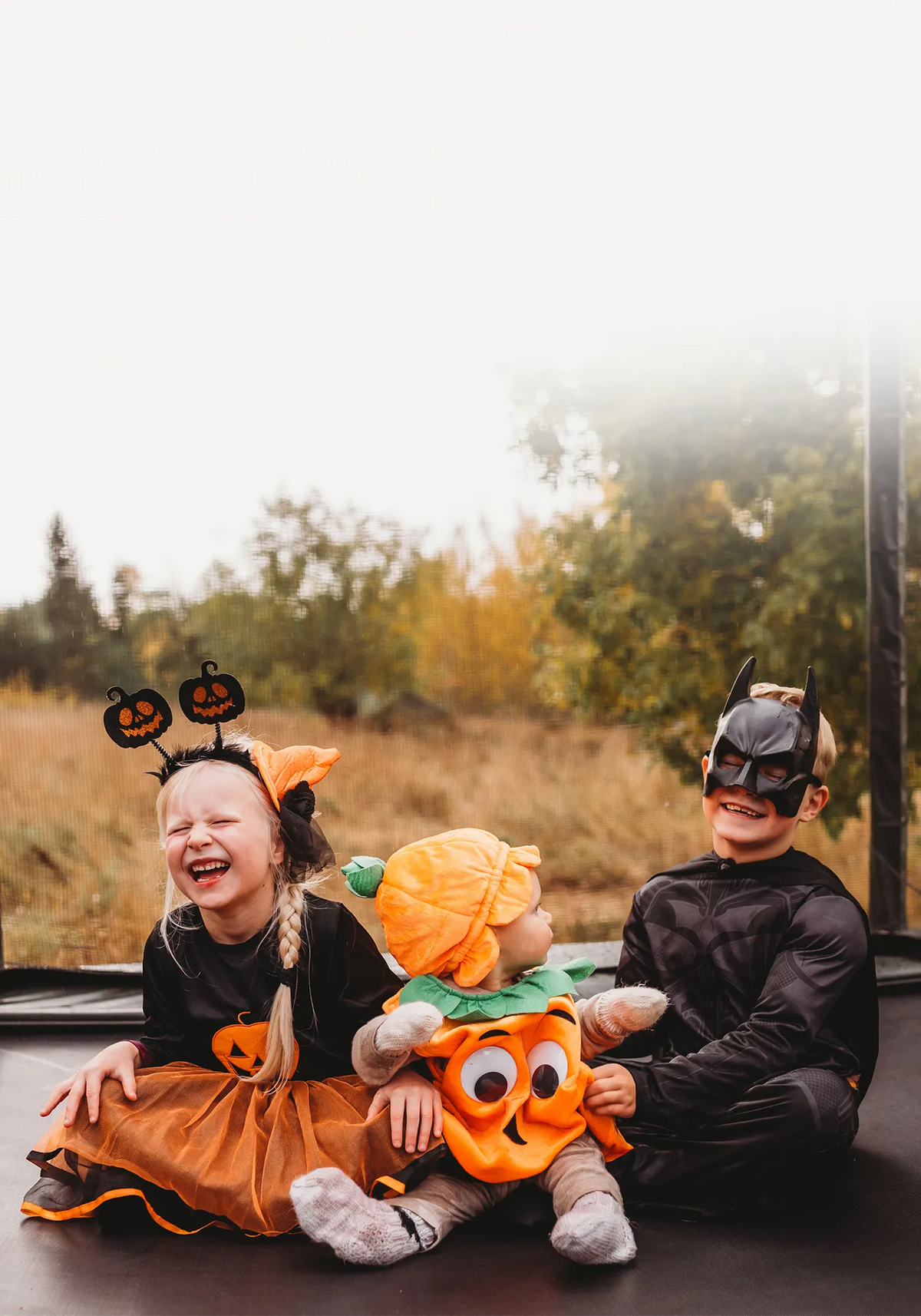 Trois enfants déguisés pour Halloween sont assis ensemble sur un trampoline ACON 16HD.