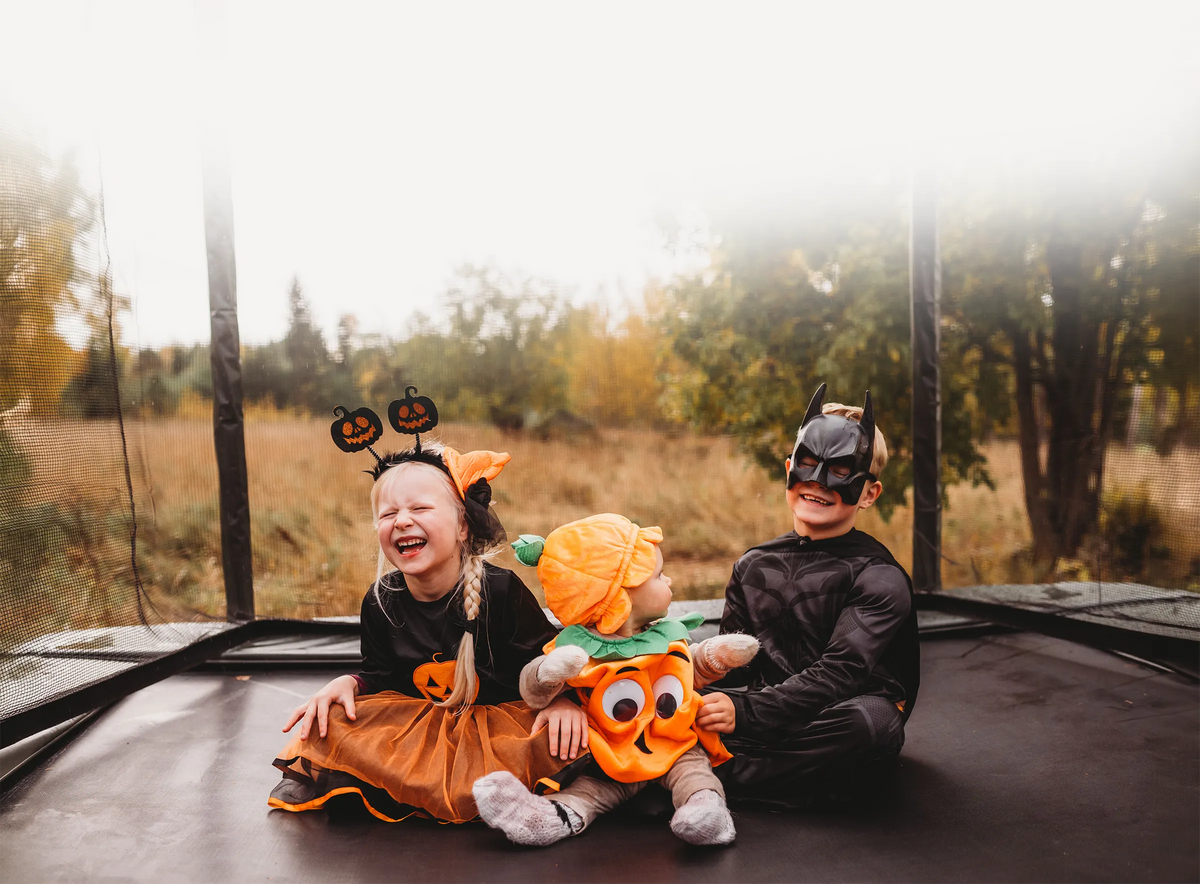Trois enfants déguisés pour Halloween sont assis ensemble sur un trampoline ACON 16HD.