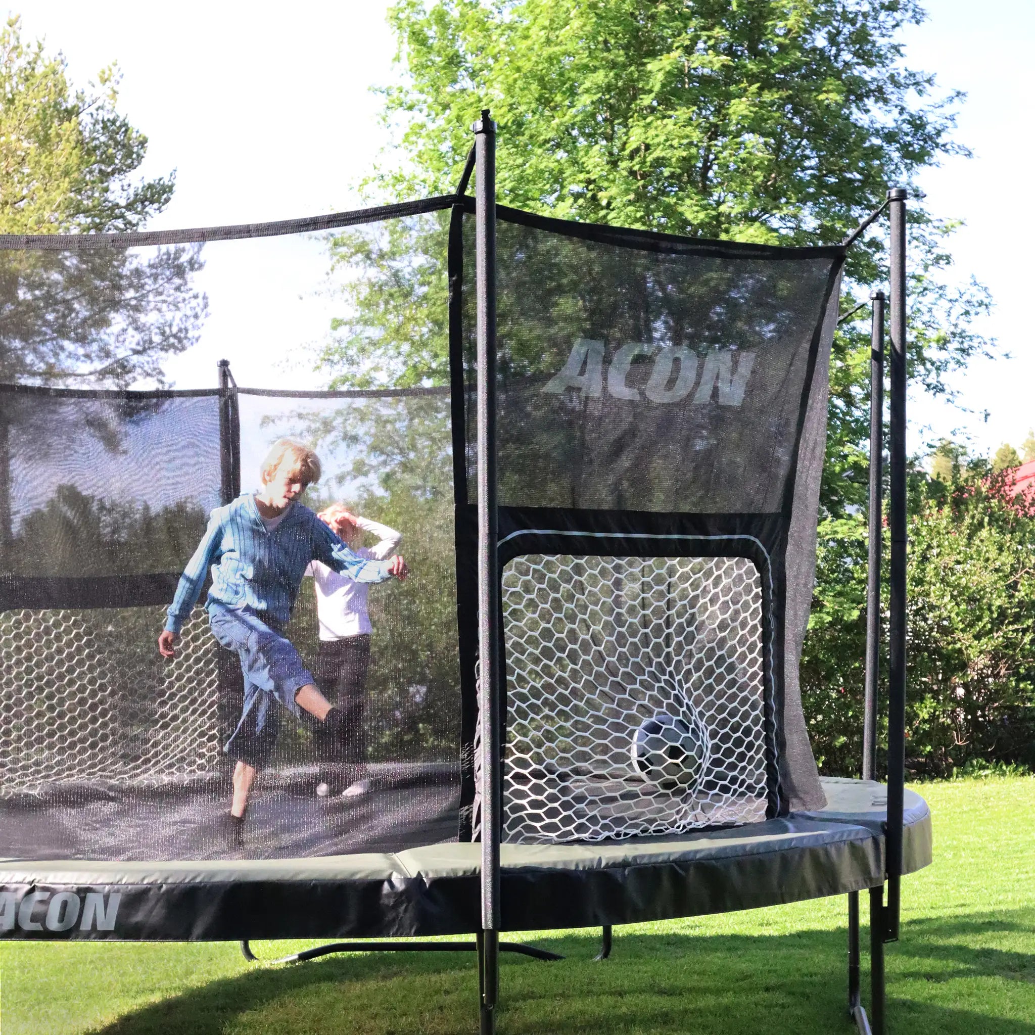 Enfants jouant au football sur un trampoline rond ACON Air sur l’herbe.