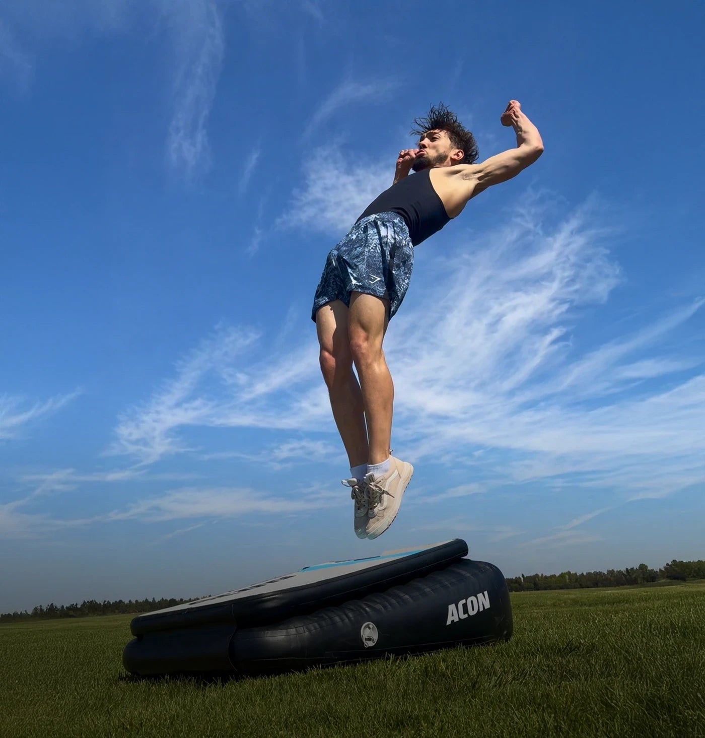 Un homme réalise un Backflip Launch sur un Acon Airboard en extérieur, l’Airboard posé sur l’herbe.