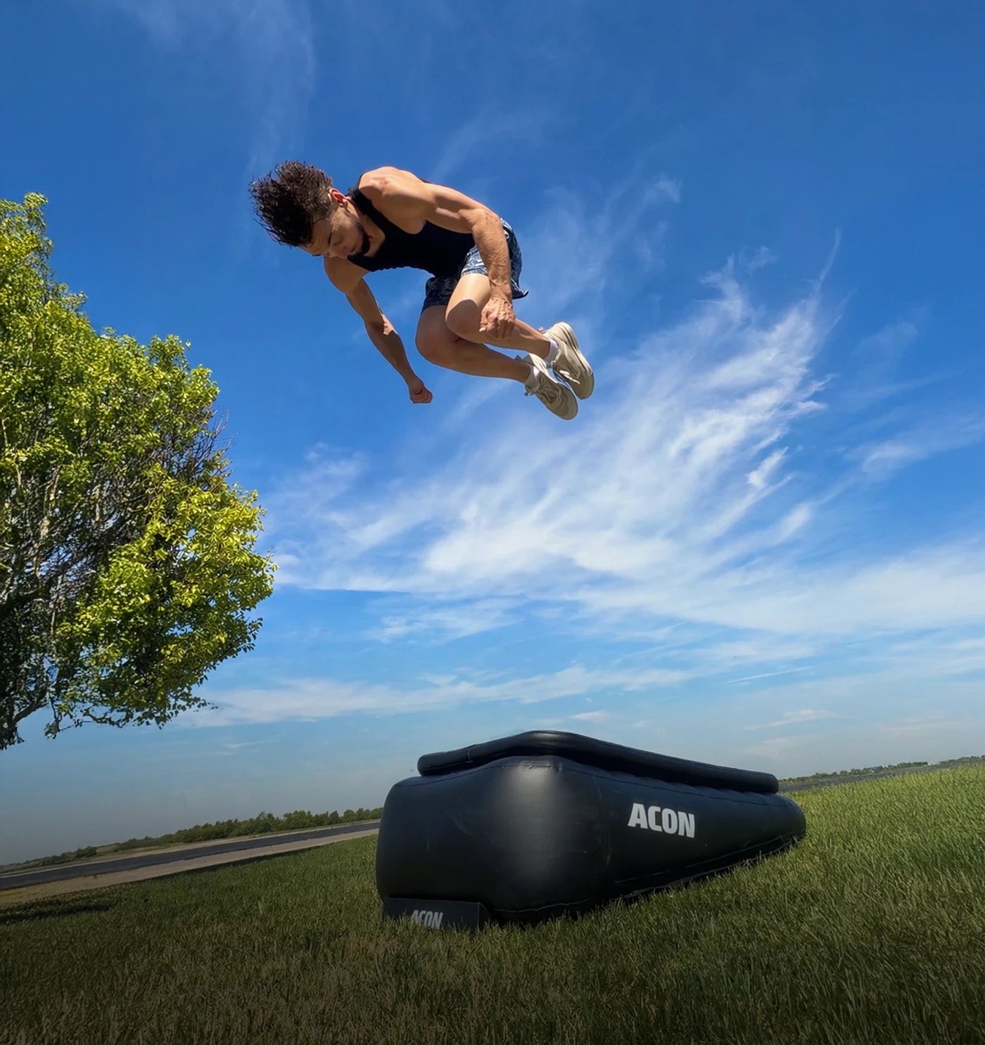 Un homme réalise un frontflip haut sur un Acon Airboard en extérieur, l’Airboard posé sur l’herbe.