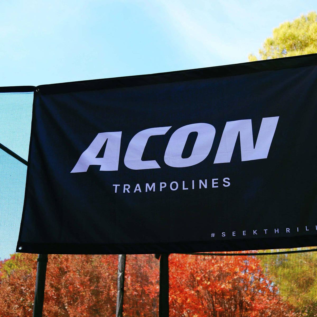 Gros plan du drapeau ACON noir sur le trampoline avec des feuilles d'arbres colorées en arrière-plan.