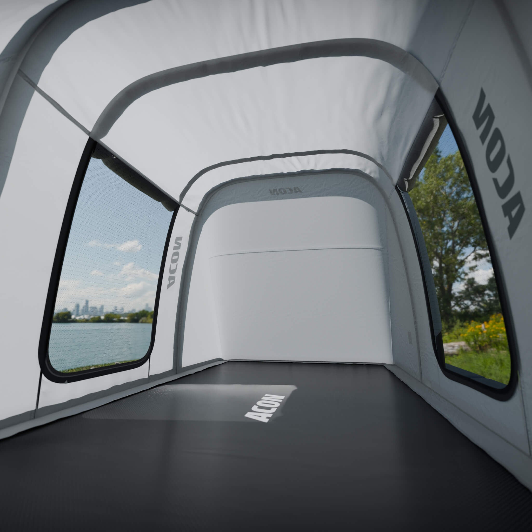 Vue de l’intérieur de la tente de trampoline Acon, montrant l’ampleur de l’espace. La tente est dotée de grandes fenêtres en filet qui offrent une vue claire sur le paysage ensoleillé du parc à l’extérieur, ce qui crée ainsi une sensation d’espace et de grandeur. 