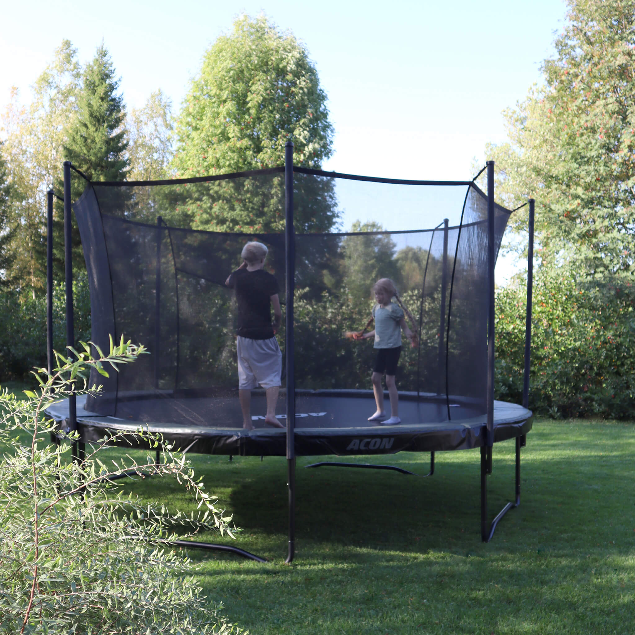 Trampoline Acon Air dans un jardin estival. Deux enfants sautent sur le trampoline.