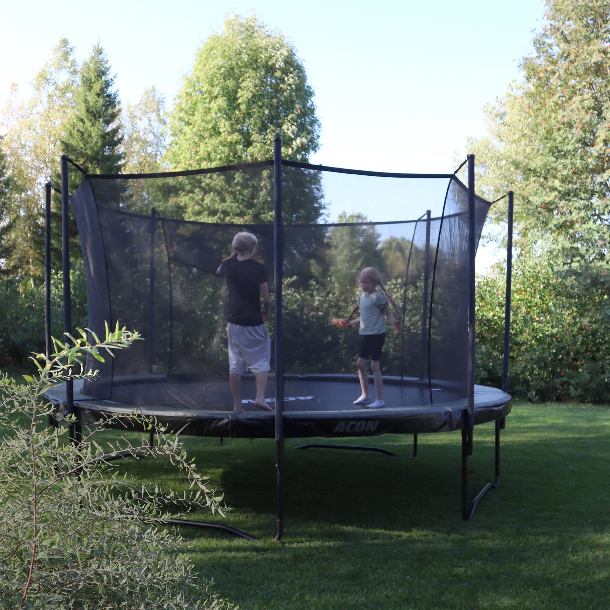 Trampoline Acon Air dans un jardin estival. Deux enfants sautent sur le trampoline.