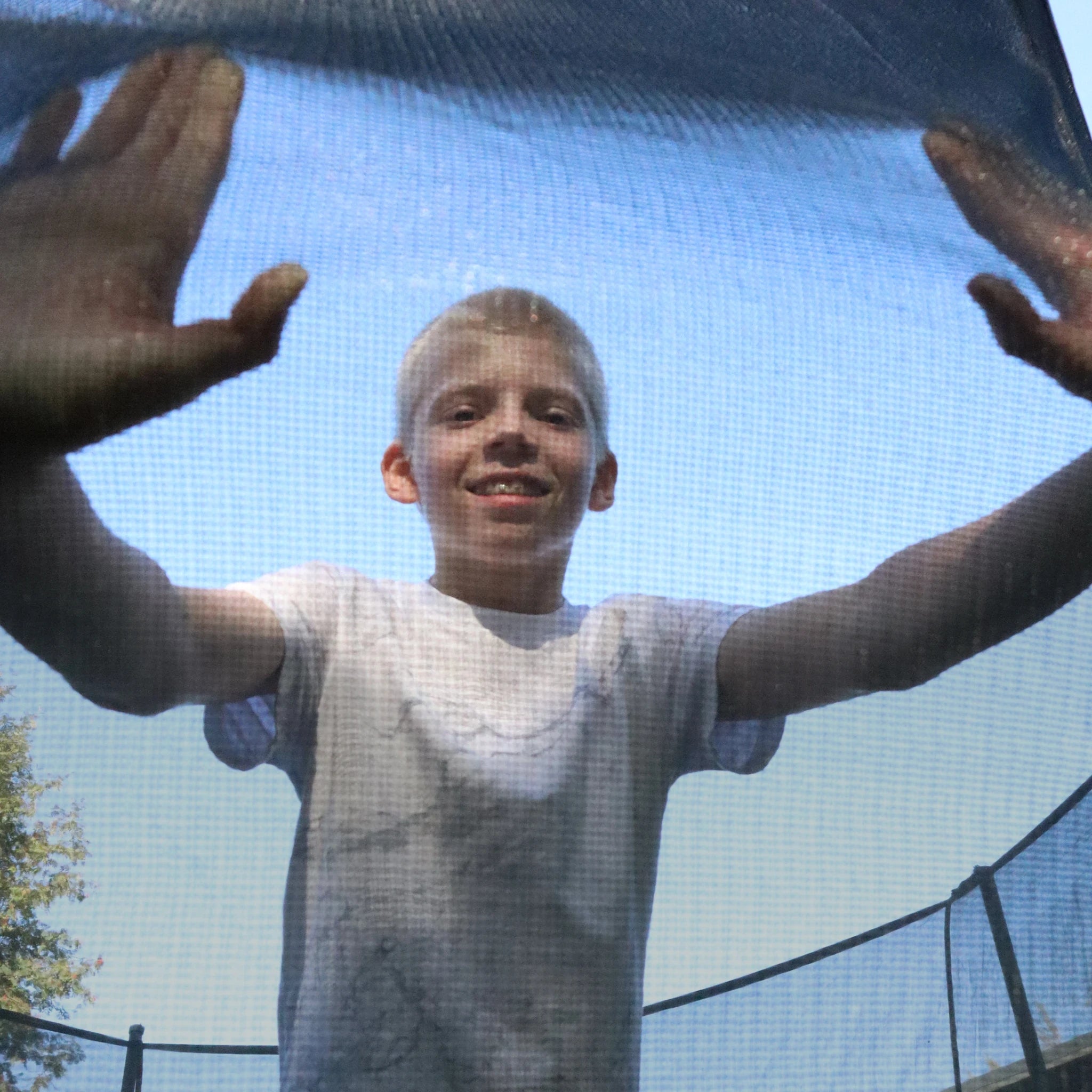 Un garçon s’appuie avec les mains sur le filet de sécurité du trampoline Acon Air.