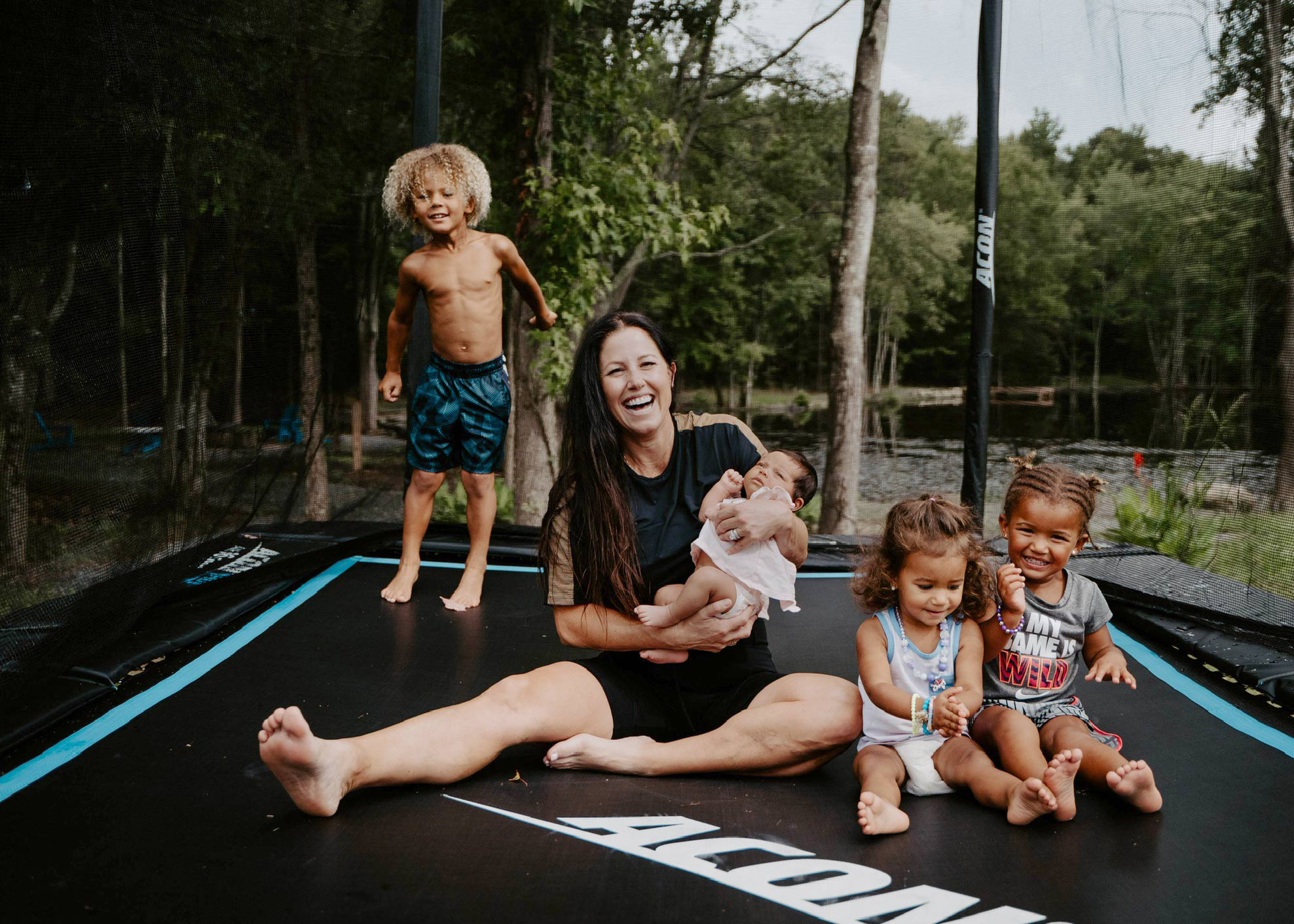 Une mère souriante, assise sur un trampoline Acon HD avec ses quatre enfants 