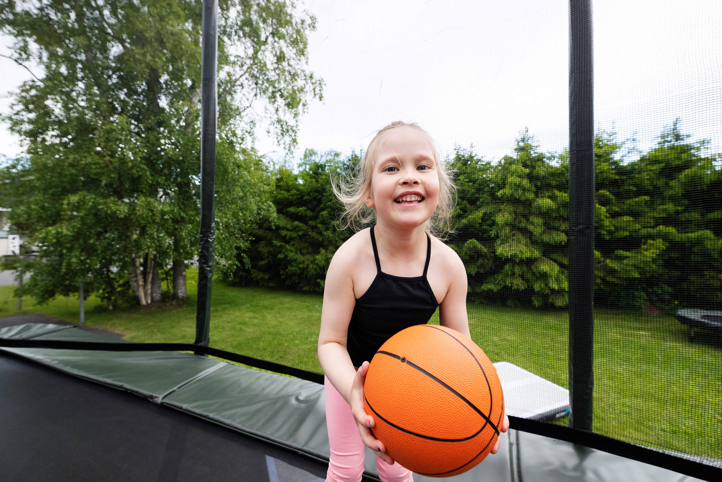 Fille heureuse sur le trampoline Acon tenant un ballon de basket sur le trampoline.