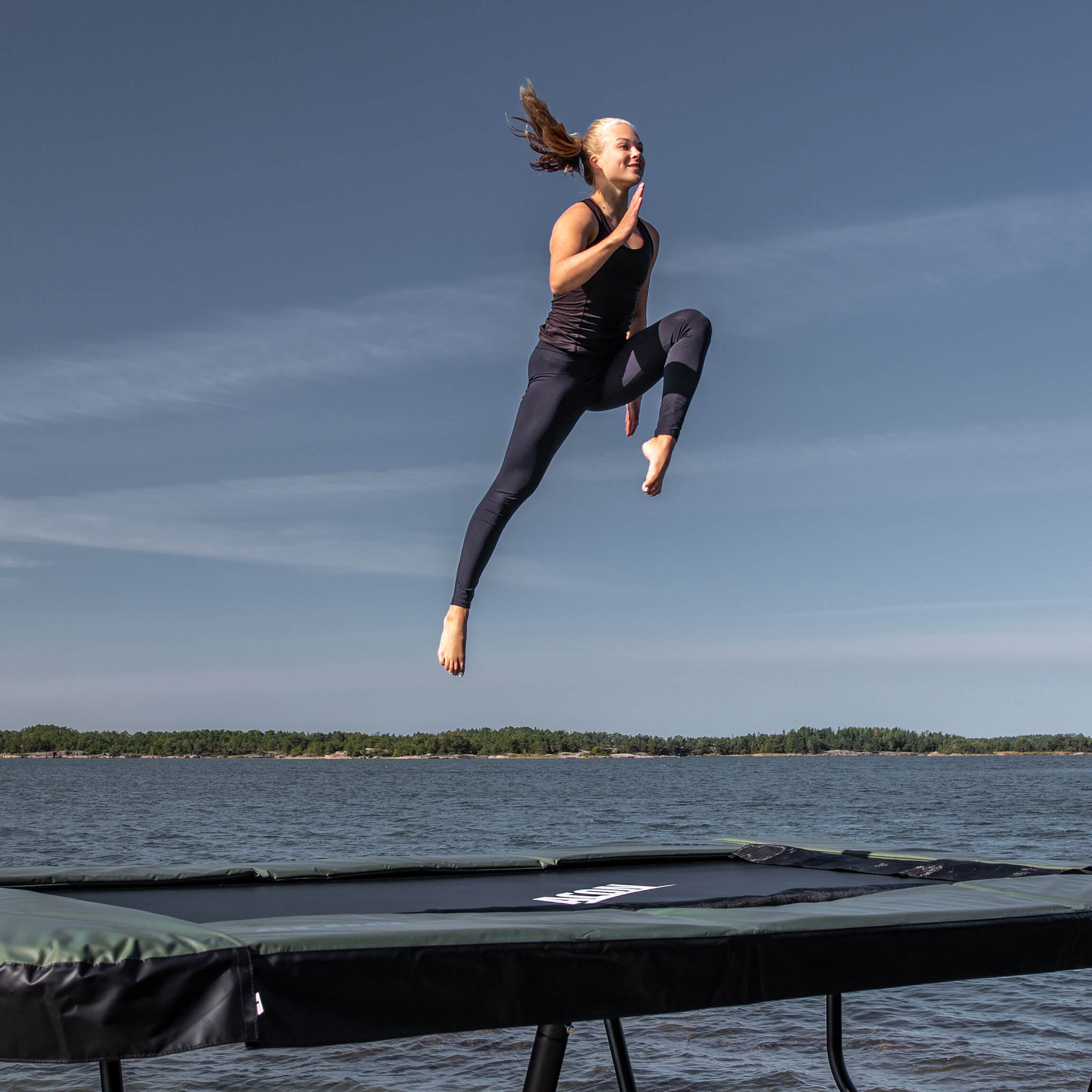 Un gymnaste saute sur un trampoline Acon 13 HD dans un paysage d'archipel.