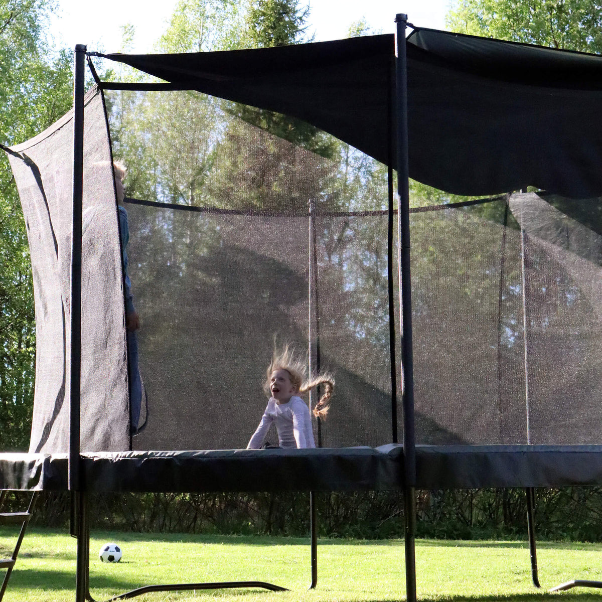 Demi-ombre fixée à un trampoline, un enfant saute en dessous.