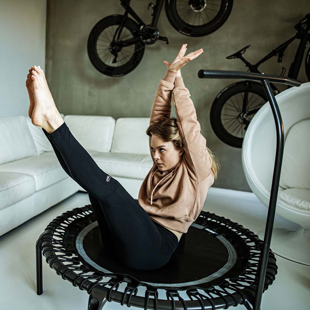 Femme faisant de l'exercice dans le salon sur un trampoline rond noir ACON FIT 1,12m.
