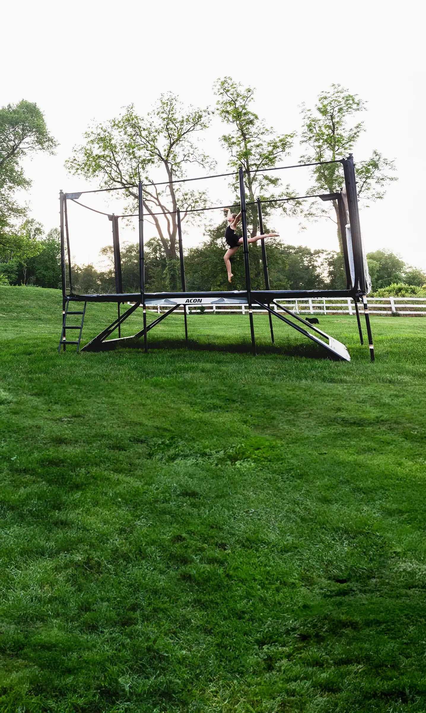 Une gymnaste saute sur un trampoline Acon X dans un jardin estival.
