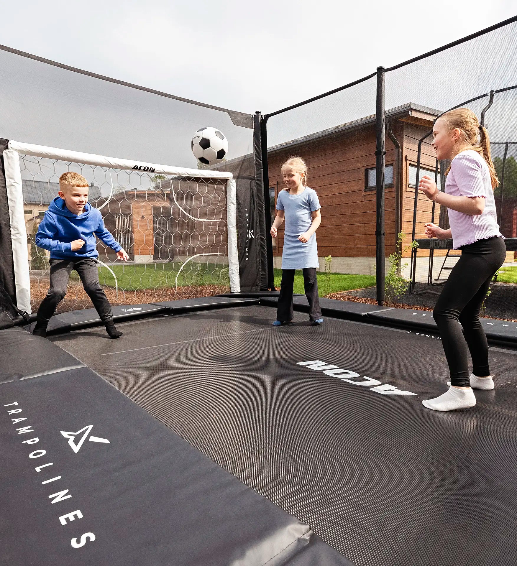 Des enfants jouent au football sur un trampoline Acon X de 17 pieds, avec un but de football en arrière-plan.