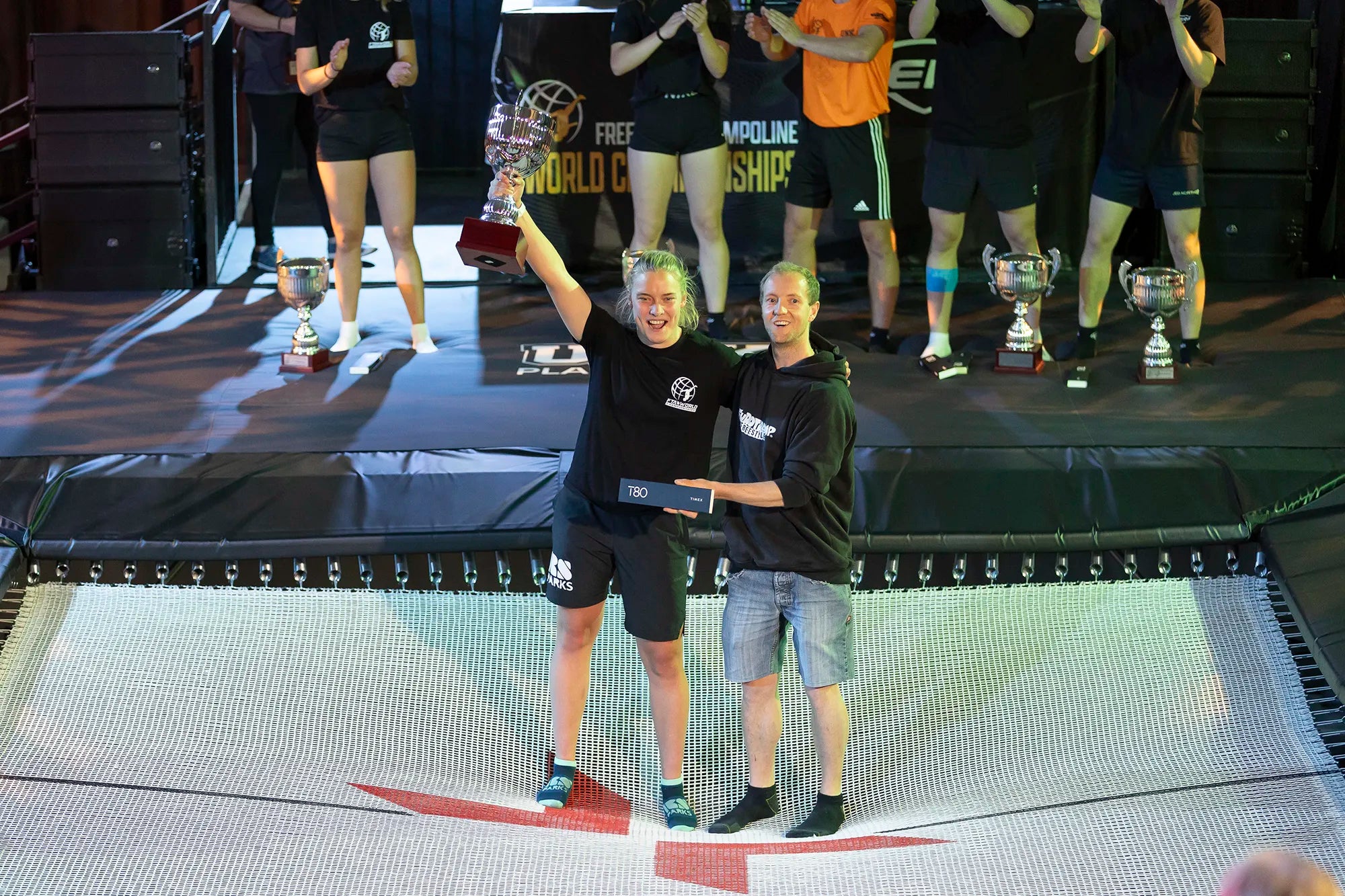 Le vainqueur du concours de trampoline tenant un trophée sur le trampoline.