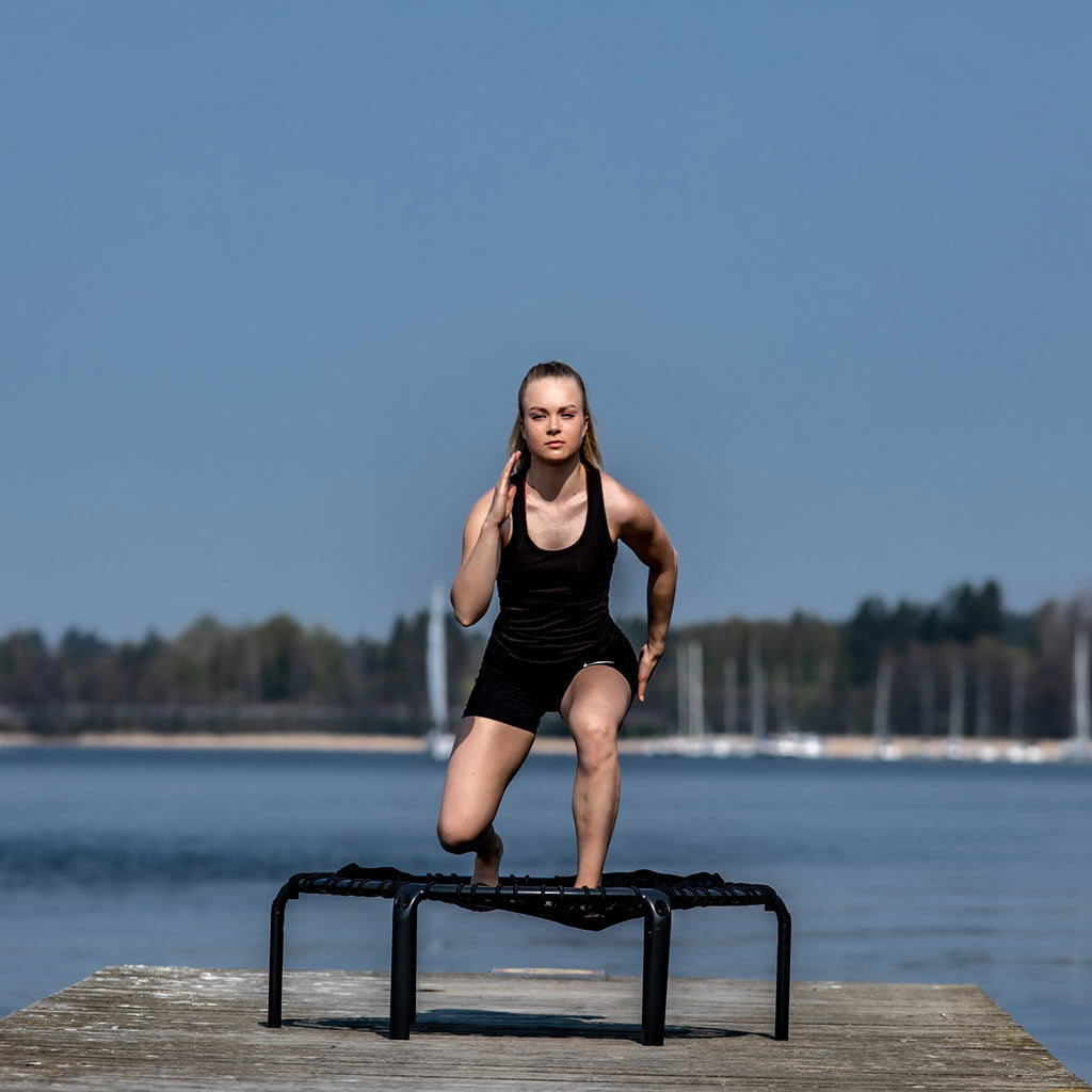 Fille s'entraînant en plein air sur le trampoline ACON FIT Hexagon au bord du lac.