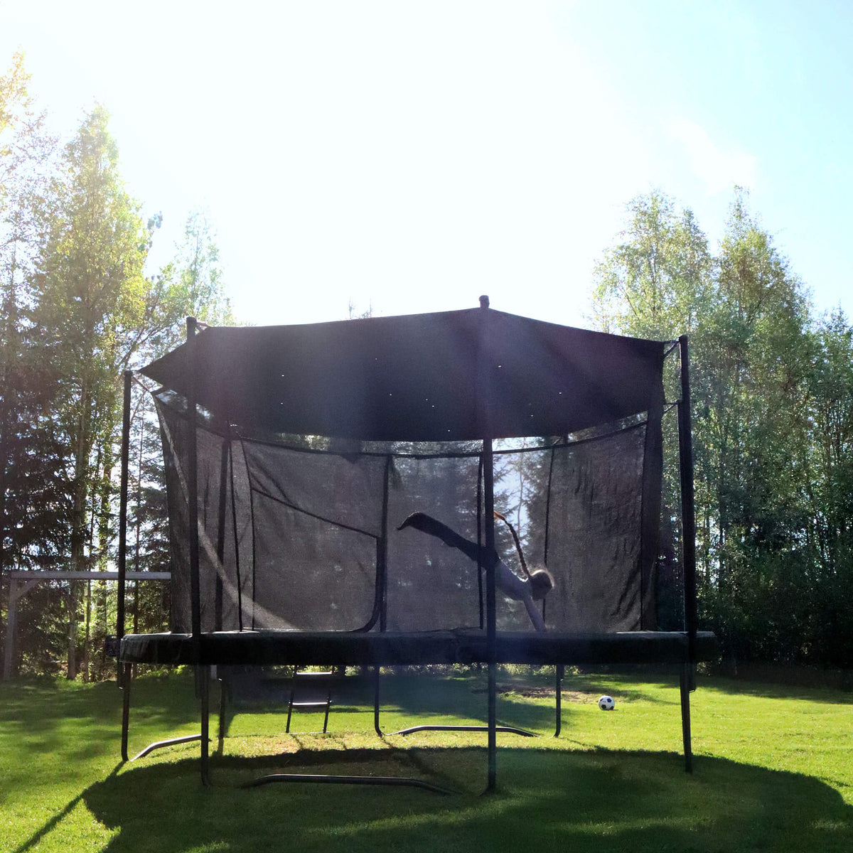 Trampoline rond Acon Air avec pare-soleil dans un environnement extérieur ensoleillé, enfant en train de sauter.