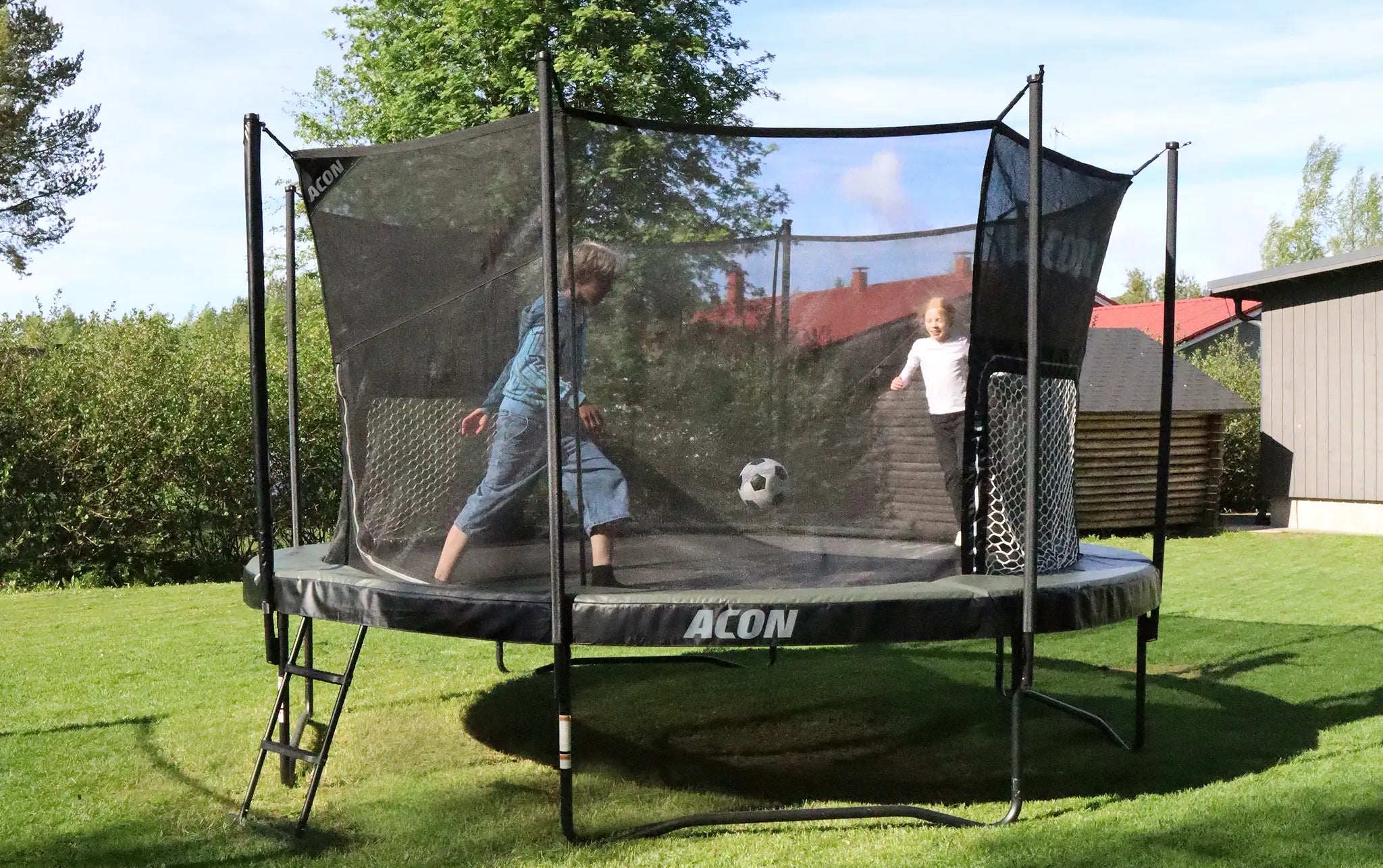 Deux enfants jouent au foot sur trampoline Acon avec filet dans le jardin.