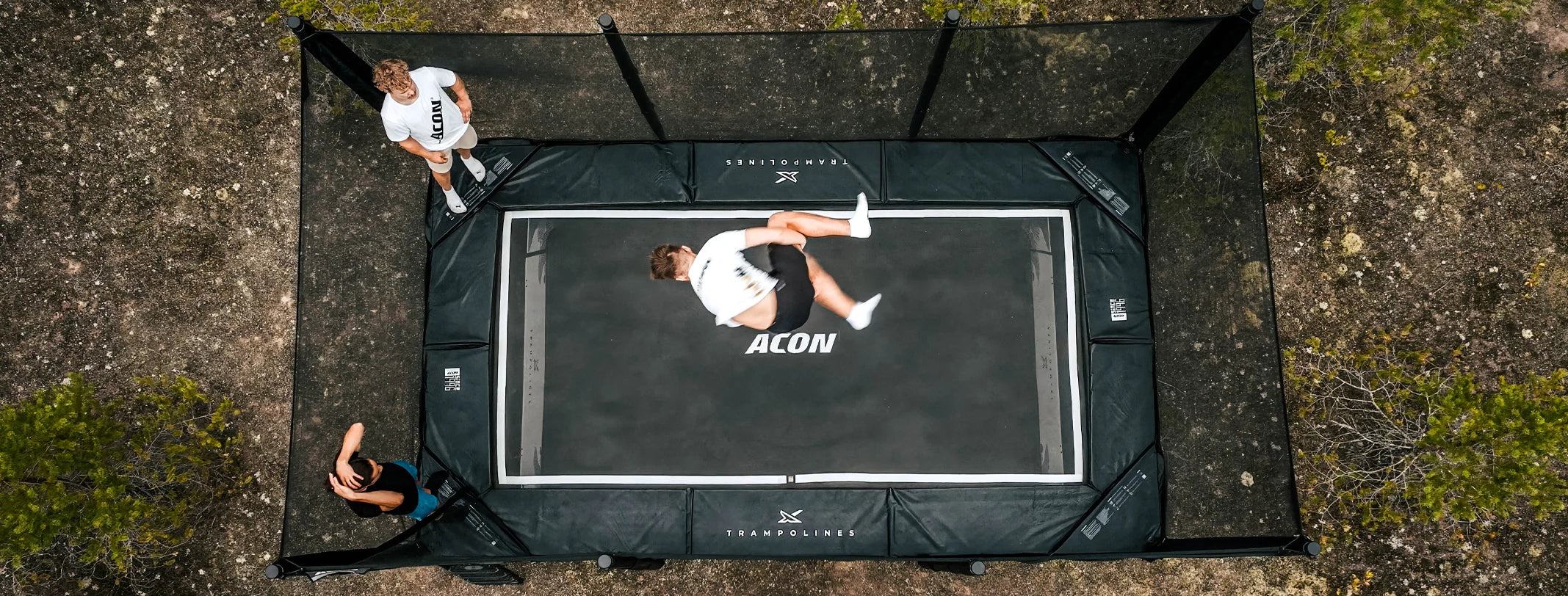 Trois personnes font des figures sur un trampoline Acon X de 17 pieds en extérieur.
