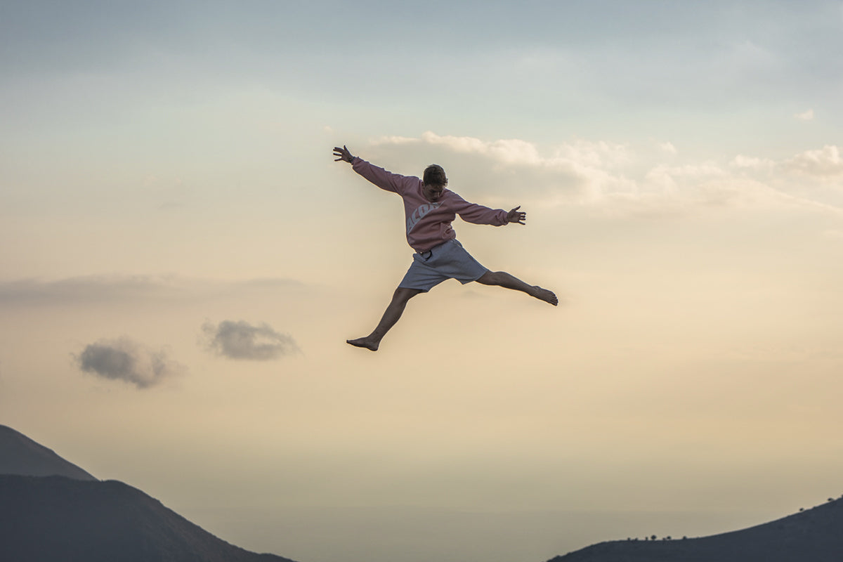Un garçon sautant dans une vue de montagne portant un sweat-shirt ACON