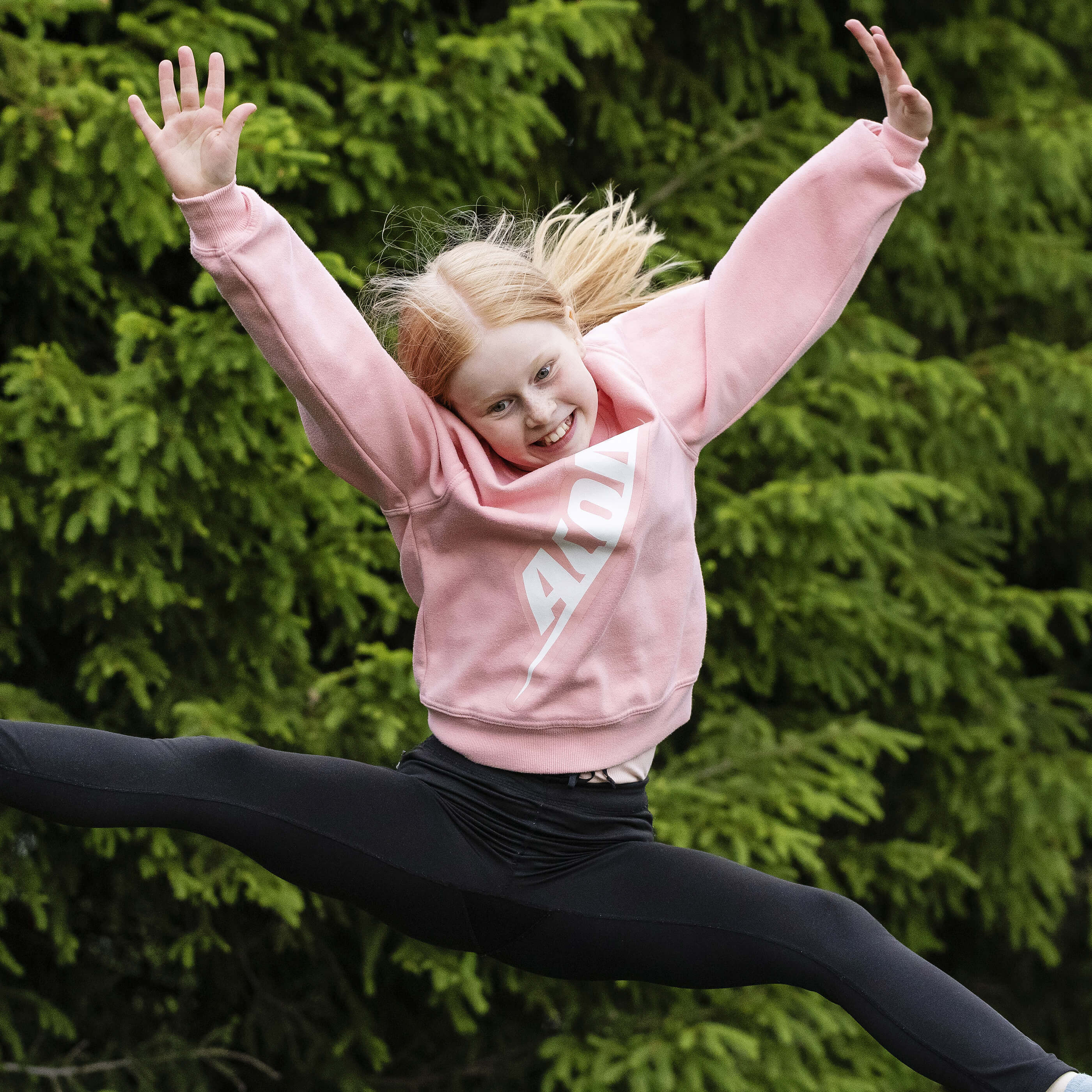 Une jeune fille heureuse, vêtue d'une chemise Acon, sautant sur un trampoline.