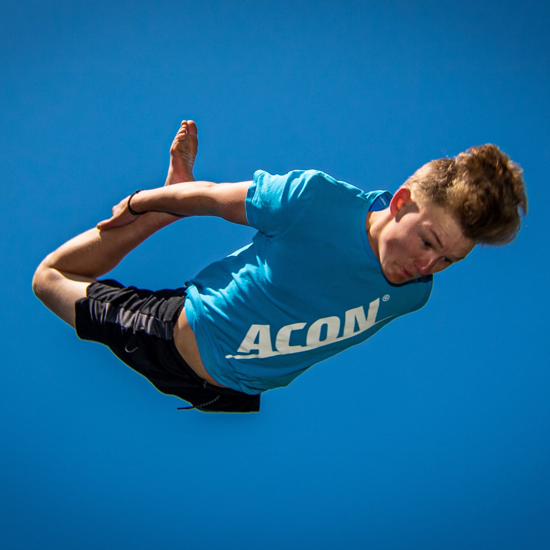 Un garçon vêtu d'un t-shirt bleu ACON effectuant un saut sur le trampoline.