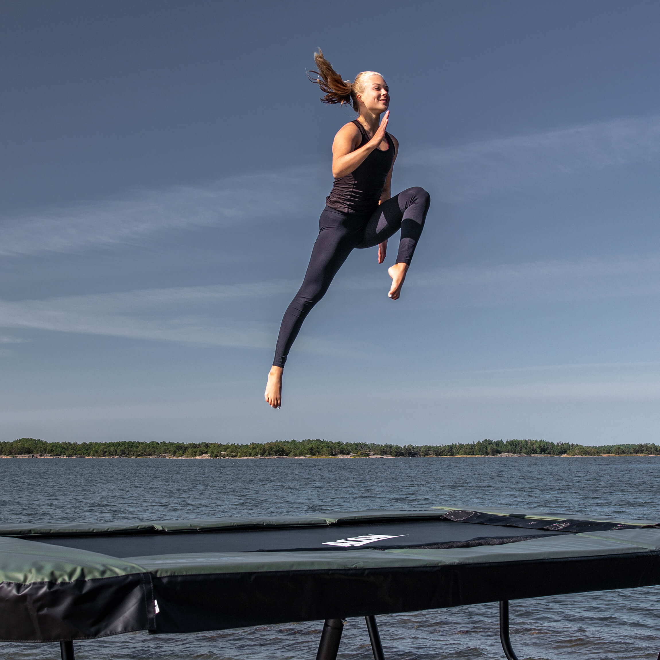 Un gymnaste saute sur un trampoline Acon 13 Sport HD dans un paysage d'archipel.