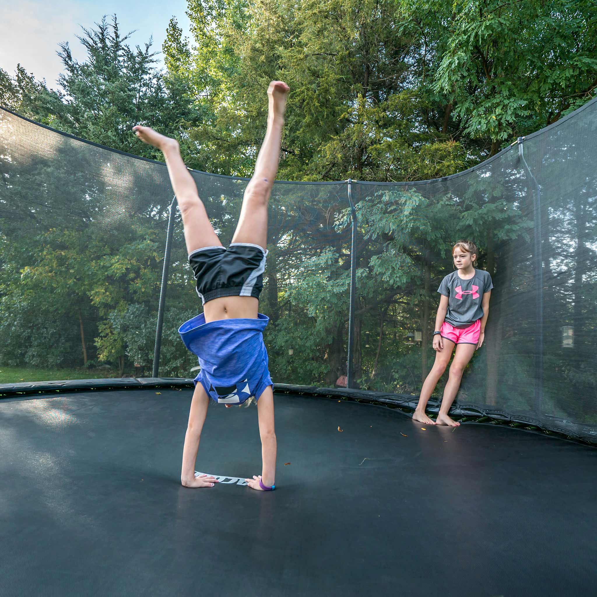 Une fille fait du handstand sur un trampoline Acon, sous le regard d'un ami.