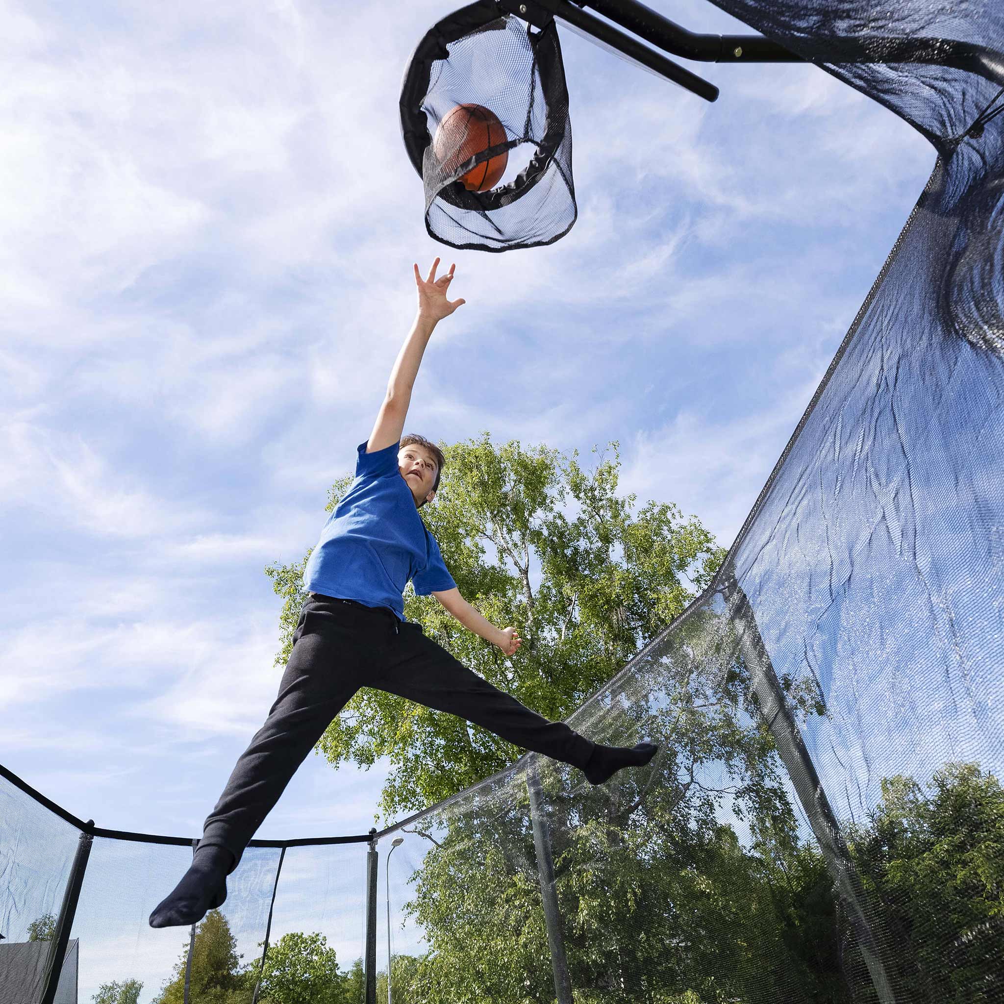 Un garçon lance un ballon de basket dans le panier de basket du trampoline.