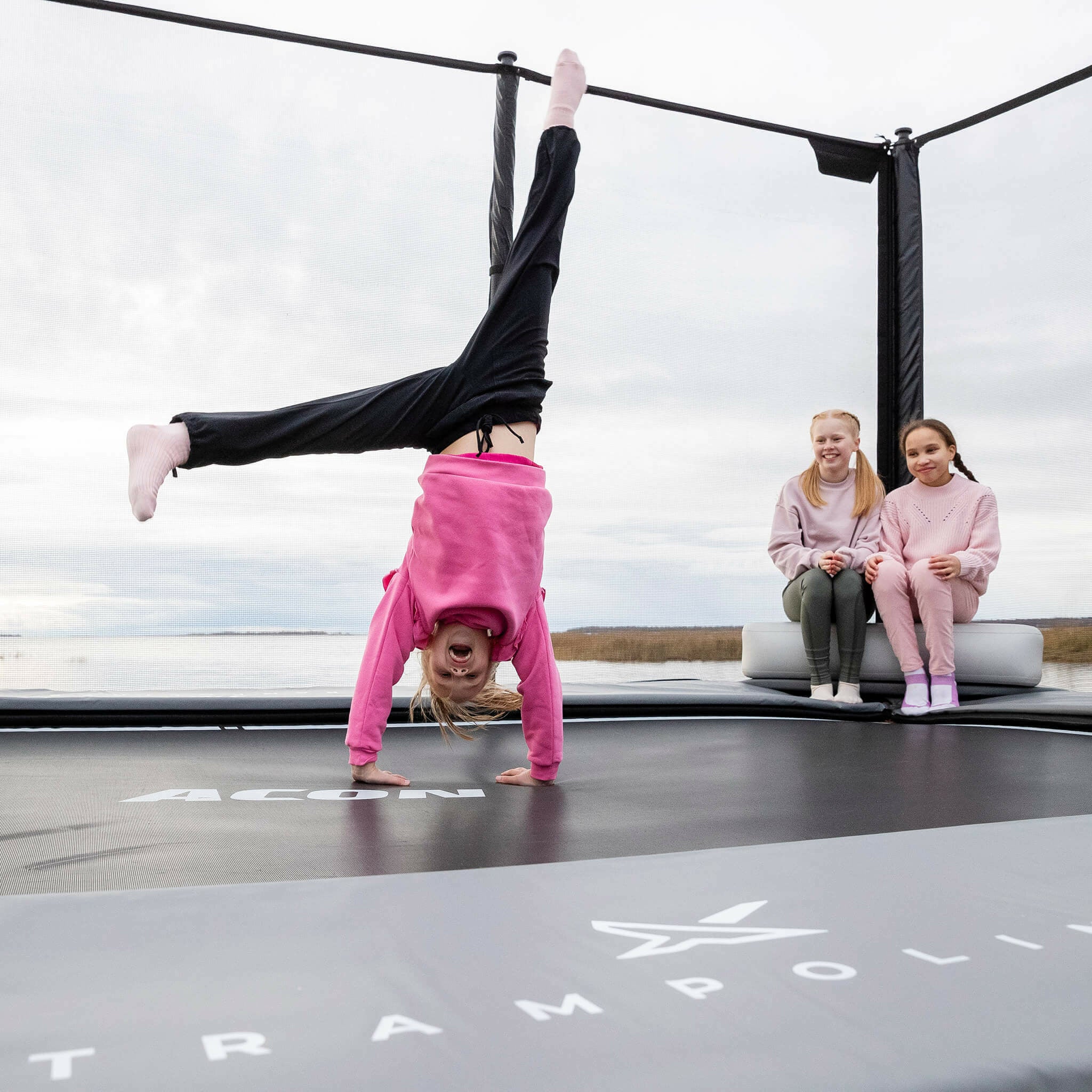 Deux filles assises sur l'Acon X Triangle Block gonflable. La fille se tient debout avec les mains sur le trampoline.